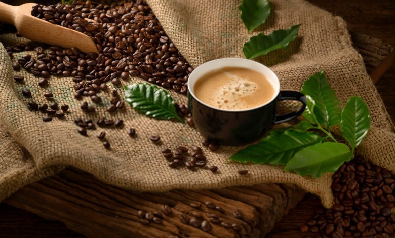 Cup of coffee with smoke and coffee beans on burlap sack on old wooden