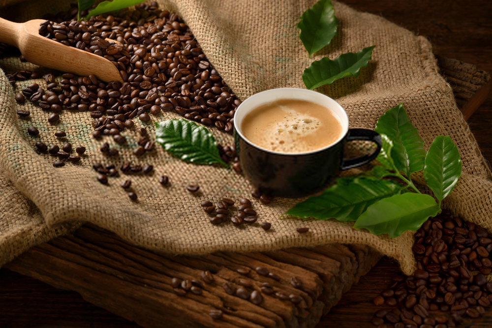 Cup of coffee with smoke and coffee beans on burlap sack on old wooden