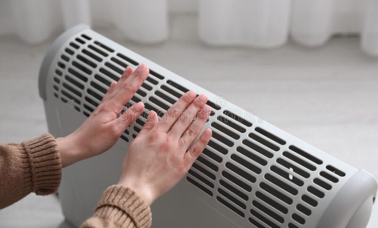 woman-warm-hands-near-electric-heater-home-closeup-211095009